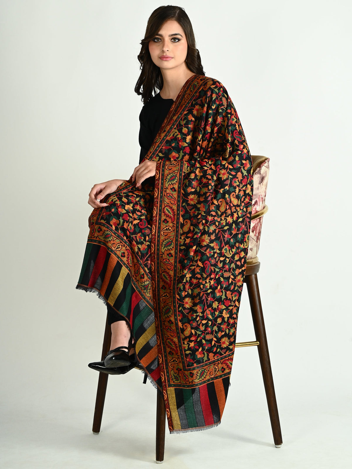 Model sitting on a chair with a colorful patterned Paisley Couture Shawl