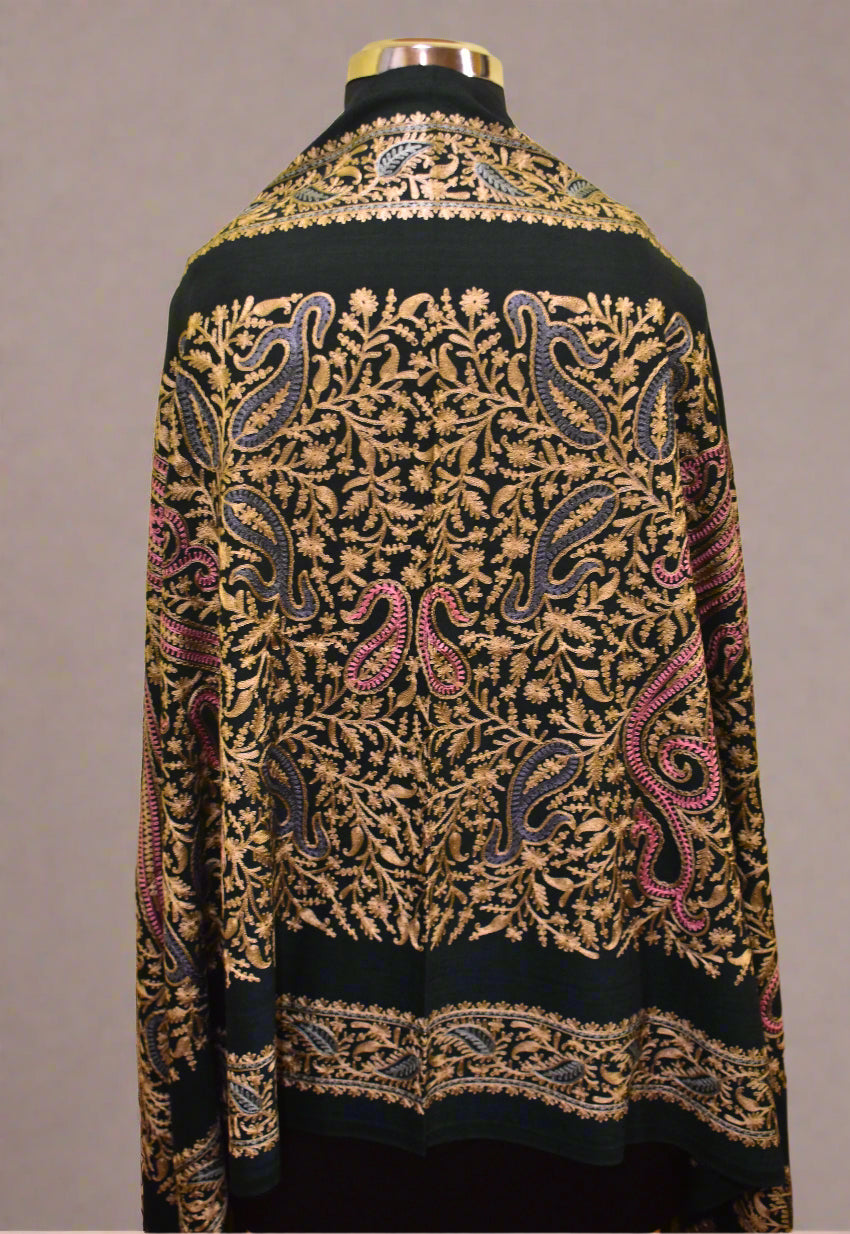 Mannequin wearing a green stole with intricate paisley patterns on a yellow wall.