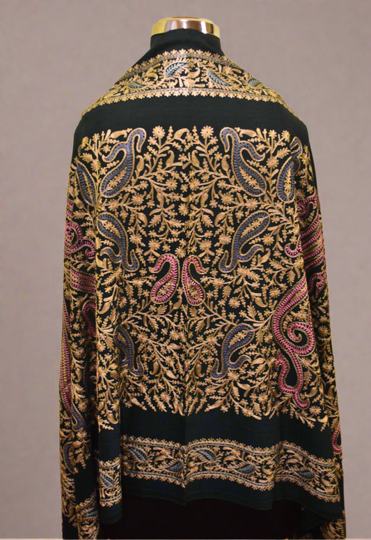 Mannequin wearing a green stole with intricate paisley patterns on a yellow wall.