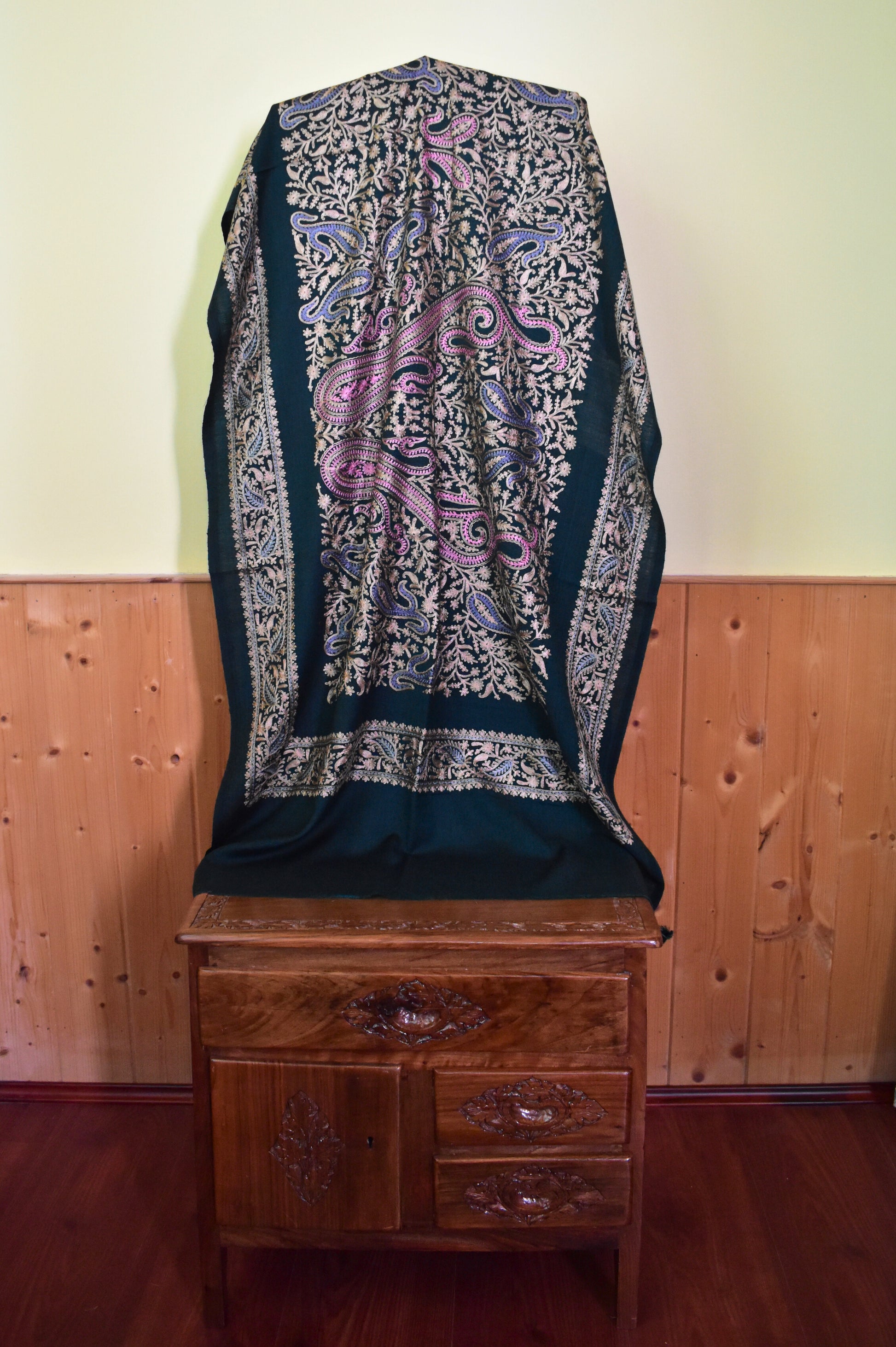 Decorative stole on a wooden chair against a wooden panel wall.